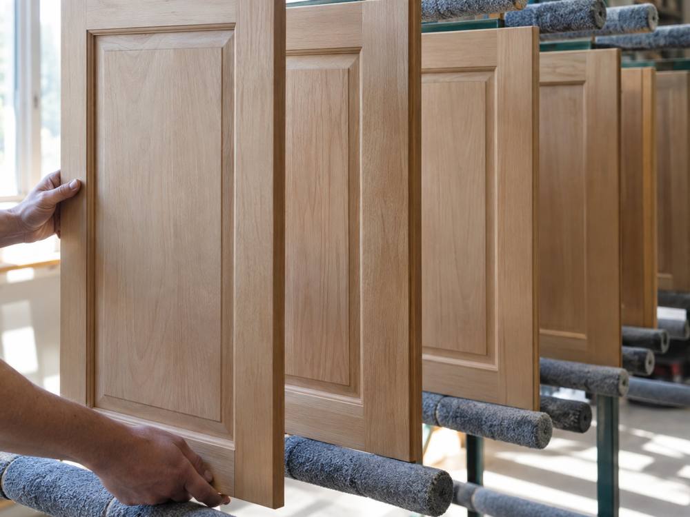 Unfinished raised-panel wood cabinet doors on a drying rack in a workshop.